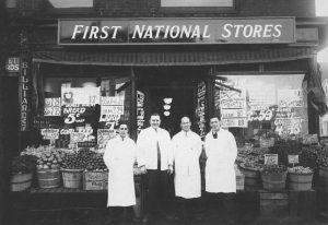 Black-and-white photograph showing four men standing outside of a storefront